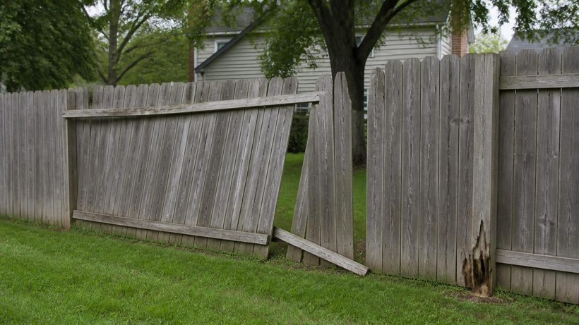 A leaning section of weathered wood privacy fence pulled away from the next run, with a rail hanging loose